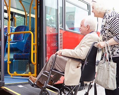 older women pushing an old man in a wheel chair into a bus